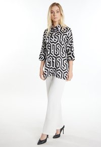 Cămașă cu model alb-negru și design geometric, cu închidere cu nasturi în față și mâneci până la cot, purtată cu pantaloni albi și tocuri negre.