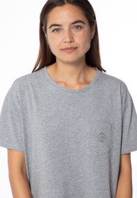 Camiseta corta gris de manga corta en tejido suave, con un cuello redondo y un pequeño logo en el bolsillo izquierdo del pecho. Corte casual y relajado.