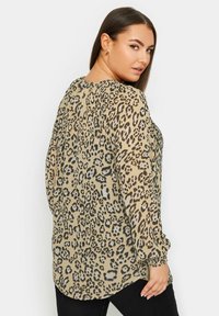 Blusa trasparente con stampa leopardata in beige, caratterizzata da maniche lunghe, scollatura rotonda e dettagli arricciati ai polsini e sul retro.
