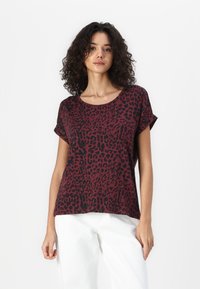 Haut à manches courtes en tissu bordeaux avec un motif léopard noir. Doté d'un col rond et d'une coupe décontractée, associé à un pantalon de couleur claire.