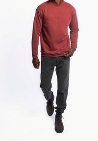 Bordeaux sweatshirt met een ronde hals en reliëflogo, gecombineerd met donkergrijze jeans en bruine laarzen. De outfit heeft een casual pasvorm en een modern ontwerp.