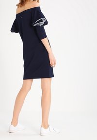 Granatowa sukienka bez ramion z falbaniastymi rękawami i rękawami o długości trzech ćwierci. Nosi się ją z białymi sneakerami, ma luźny krój i miękką teksturę.