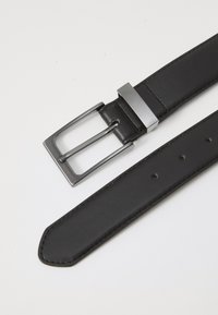 Cinturón de cuero negro con una hebilla rectangular de metal plateado. La correa presenta una textura suave y múltiples agujeros para ajustar el tamaño.