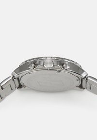 Montre en acier inoxydable argenté avec un boîtier rond, deux poussoirs et une lunette texturée. Bracelet lisse avec un fermoir sécurisé. Dos gravé.