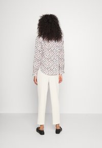 Chemise à manches longues à motifs floraux dans des couleurs claires, associée à un pantalon crème et des chaussures noires. Vue de dos mettant en avant les détails de conception.