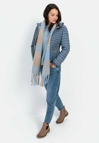 Blå pufferjakke med hætte, lyseblå sweater og lyseblå-beige stribet tørklæde. Båret med blå jeans og brune ankelstøvler.