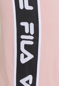 Różowy materiał z czarno-białymi pionowymi paskami i wyraźnym napisem "FILA" w kontrastującym kolorze. Gładka tekstura, casualowy styl.