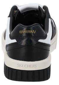 Black and white sneaker with a textured black upper, white accents, and a cream rubber sole. Features golden stitching and logo on the heel.