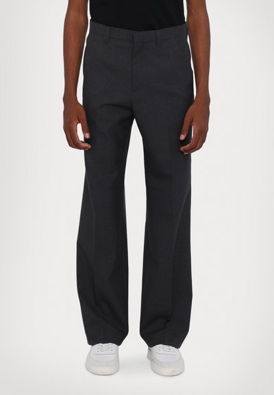 Pantalons tailleurs gris foncé à coupe droite, fabriqués en tissu lisse, avec des passants de ceinture et des poches latérales, associés à des baskets blanches.