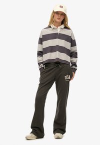 Gestreept grijs en marineblauw shirt met lange mouwen en een witte kraag, gecombineerd met olijfgroene joggingbroek met de tekst "USA" in crèmekleur. Witte pet en sneakers.