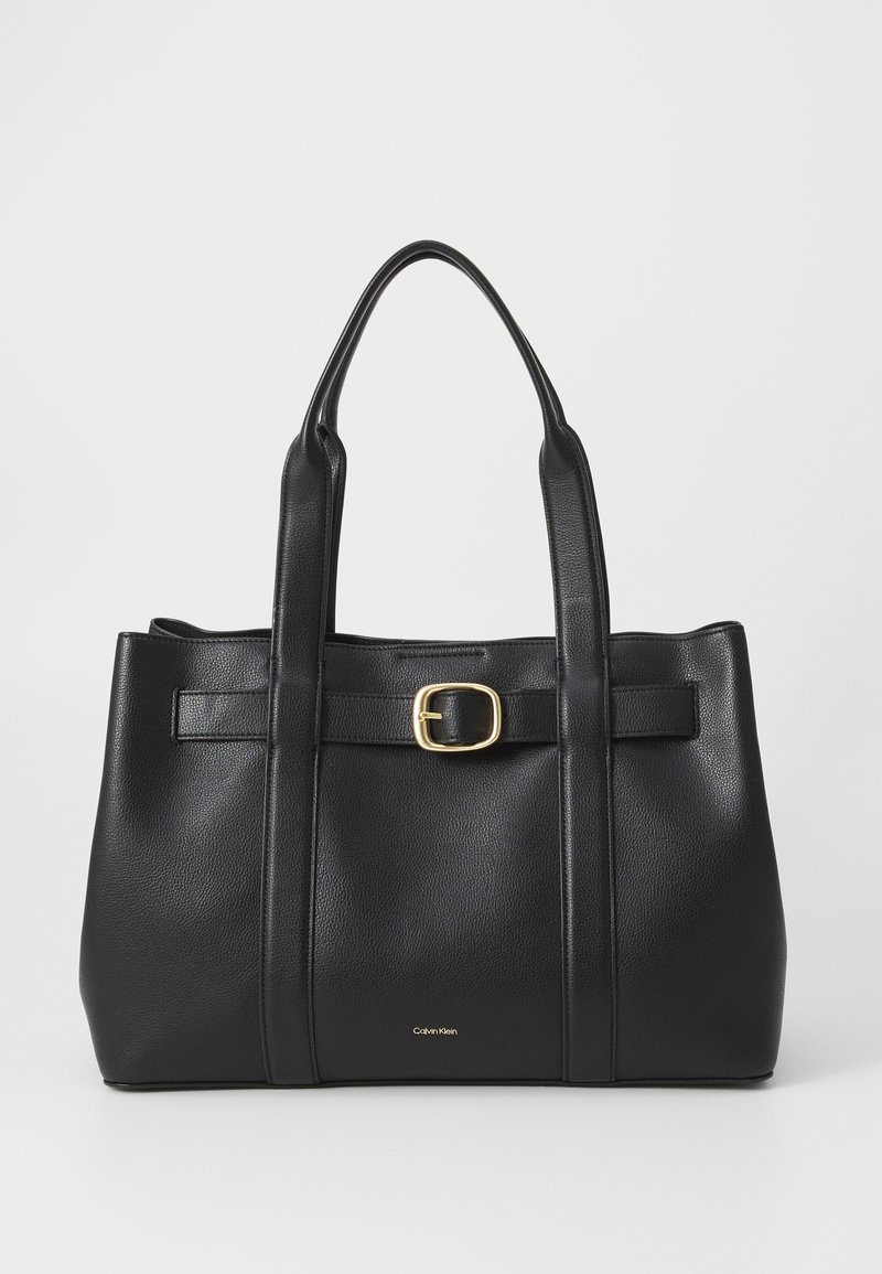Czarna skórzana torba tote z dwoma solidnymi uchwytami, prostokątny kształt, centralny detal z klamrą oraz subtelne logo. Teksturowana powierzchnia, minimalne akcenty.