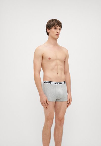Boxers cinzentos de algodão com uma cintura preta com o logotipo da Moschino. O design apresenta um ajuste justo e uma textura suave. O modelo está de perfil.