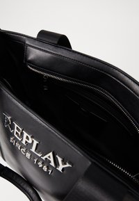 Svart skinn toteveske med sølv "REPLAY"-logo. Har glidelåslommer og et teksturert håndtak for godt grep. Innvendig er den fôret i svart.