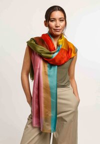 Foulard in seta con strisce verticali verdi, arancioni, rosa, blu e marroni, appoggiato sulle spalle di un modello, texture liscia.