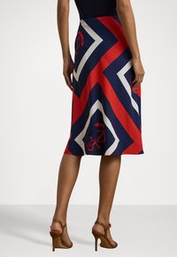 Hame polyester yang menampilkan pola chevron merah, navy, dan putih dengan aksen nautikal. Desain panjang sedang dengan tekstur yang halus.