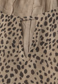 Beige stof met een onregelmatig donkerbruin luipaardprintpatroon en een kleine V-vormige inkeping bij de halslijn.