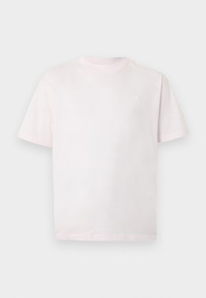 Jednostavna svjetloružičasta majica kratkih rukava s okruglim izrezom i malim bijelim logotipom na lijevoj strani prsnog dijela, prikazana na sivoj pozadini.