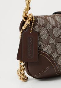 Brown Coach bag with signature "C" pattern, gold chain strap, leather tag embossed with brand name, and gold clasp detail.