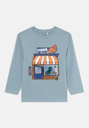 Light blue long-sleeve shirt with cartoon pizza shop illustration featuring a giant pizza slice sign, striped awning, and a creature eating inside.