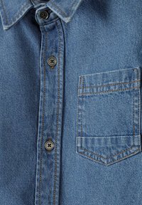 Világoskék farminging klasszikus gallérral, gombos záródással és mellzsebbel. Kontrasztos narancssárga varrással a varratok mentén.