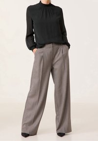Schwarze Bluse mit gerafftem Ausschnitt und langen Ärmeln, kombiniert mit hoch taillierten, karierten weit geschnittenen Hosen mit vorderen Falten.