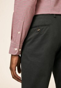 Czerwona i biała koszula w kratę z mankietami na guziki, zestawiona z ciemnoszarymi spodniami z tylną kieszenią i zdobieniem na guziki.