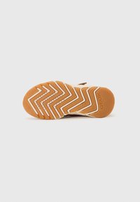 Semelle de chaussure marron avec un motif géométrique en zigzag de couleur crème clair et orange. Présente des trous de drainage et un logo sur le côté pour la ventilation.