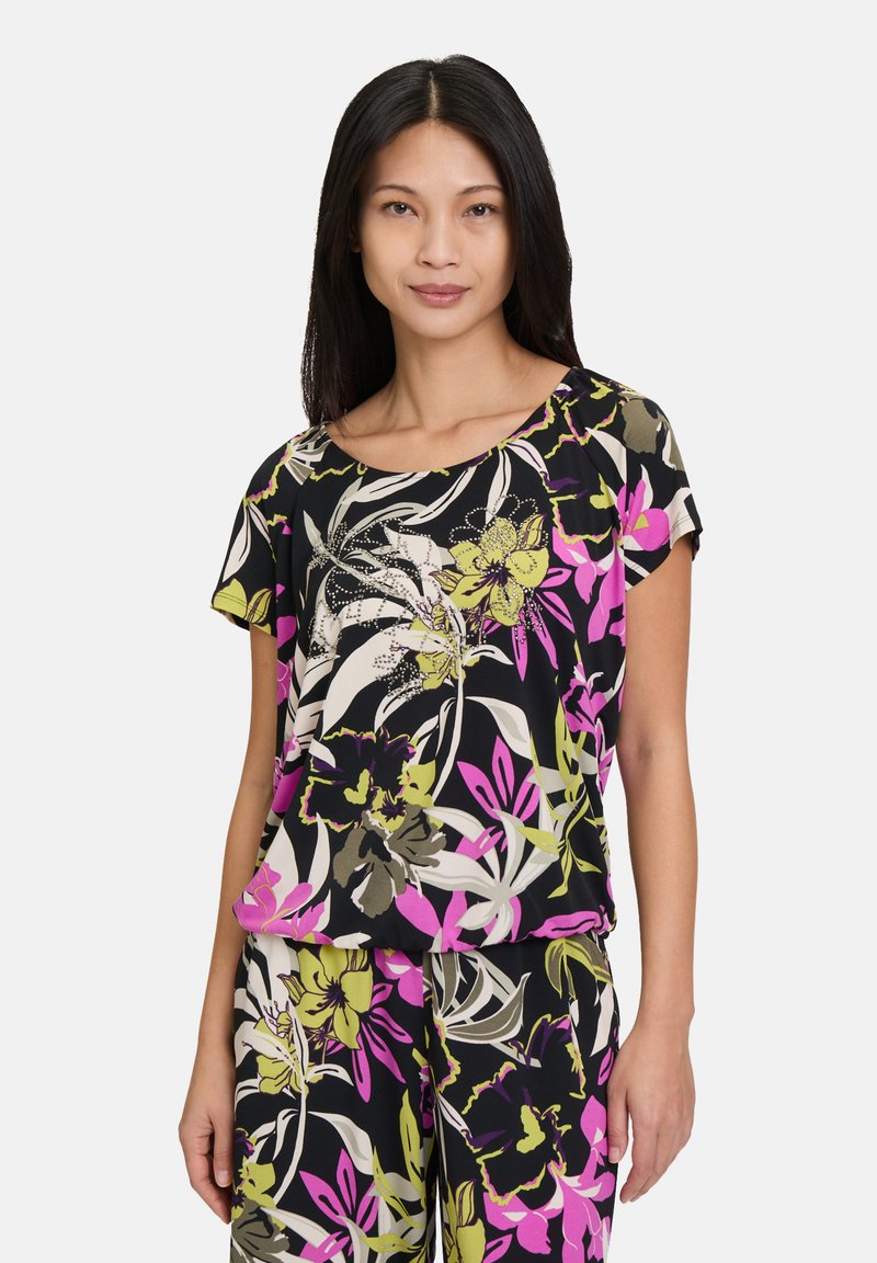 Blouse noire à motifs floraux avec des motifs audacieux en rose, vert et blanc. Tissu léger avec des manches courtes et un col arrondi, assorti à un pantalon.