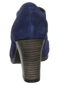 Mörkblå mockaskor med hög klack, en strukturerad, staplad träklack och en slät bakdel. Har diskreta sömnadsdetaljer.