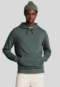 Groene hoodie gemaakt van zacht materiaal, met een kangoeroezak, trekkoord en een klein geborduurd logo op de borst.