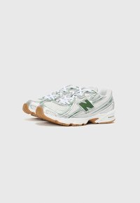 Chaussures de sport avec une tige en mesh argenté et vert, dotées de lacets blancs, d'une semelle rembourrée et d'une semelle extérieure en caoutchouc gomme texturée.