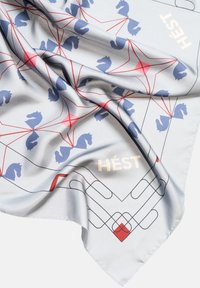 Silkesjal som har en lys grå bakgrunn, blå hestelimbo, røde geometriske linjer og ordet "HÉST" i gull.