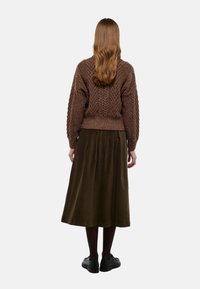 Un pull en laine marron avec un design texturé, associé à une jupe plissée jusqu'aux genoux de couleur vert foncé. Des chaussures noires complètent la tenue.
