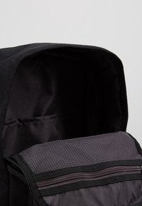 Svart ryggsäck med huvudfacket öppet, som visar svart inredning och en grå nätficka med dragkedja på framflappr.