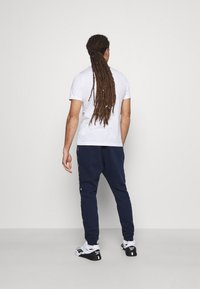 Bílá trička a námořnické tepláky. Tričko má krátké rukávy; tepláky mají boční prvky a manžety na konci nohavic. Obuv: černobílé tenisky.