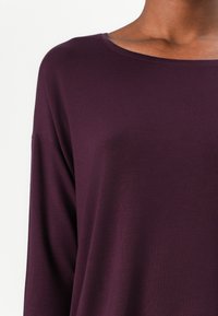 Burgunderfarget langermet topp med vid halsringning, laget av glatt, elastisk stoff. Designet har en avslappet passform og subtil glans.