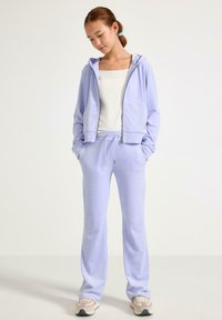 Lys lilla lynlås-hættetrøje med to forlommer, stylet med matchende joggingbukser. Glat stof med snøre i taljen. Sneakers med polstring.