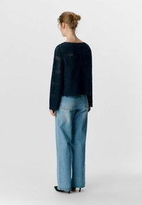 Pull en tricot noir ajouré avec un design cropped, des manches longues et un ourlet festonné, associé à un jean large bleu clair et des talons noirs.