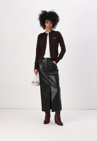Brun cardigan, hvit skjorte, svart skinn maxi skjørt med slisse, og brune hæler. Rosa håndveske gir et kontrasterende accent.