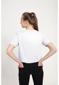 T-shirt bianca in cotone con maniche corte, scollatura rotonda e vestibilità morbida, abbinata a jeans neri a taglio aderente. Vista da dietro.