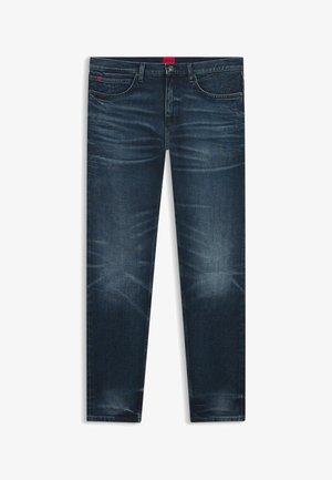 Jean slim bleu foncé avec détails délavés, design à cinq poches, fermeture par bouton et fermeture éclair, et une petite étiquette de marque rouge sur la ceinture.