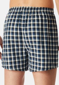 Boxers à carreaux bleus et blancs avec une taille élastique et une coupe ample. Le tissu semble doux avec une texture légère et respirante.