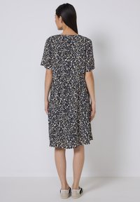 Kurzärmliges navy-blaues Kleid mit einem cremefarbenen, abstrakten Blättermuster, tailliertem Gürtel und relaxed Schnitt, kombiniert mit hellen Slippers.