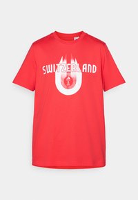 Rød bomulds t-shirt med "SWITZERLAND" i hvide bogstaver, med et cirkulært grafisk design, der inkorporerer det schweiziske logo. Korte ærmer.