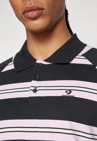 Svart och rosa randig polo skjorta med svart krage, med tre knappar och en liten broderad logotyp på vänster bröst.