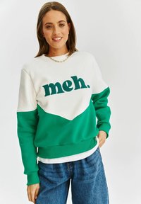 Zelená a bílá mikina se slovem "meh." v barveném blokovém designu a žebrovanými manžetami. Měkký materiál s uvolněným střihem.