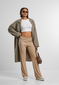Károvaný oversized kabát, bílý cropped top, béžové široké kalhoty, hnědá kabelka, šedé tenisky. Obsahuje měkké textury a neutrální barvy.