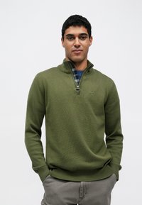 Πράσινο πουλόβερ ελιάς με γιακά με φερμουάρ και καρό επένδυση, διαθέτει ριμπ μανσέτες και τελείωμα, κατασκευασμένο από υφασμάτινο πλεκτό ύφασμα.