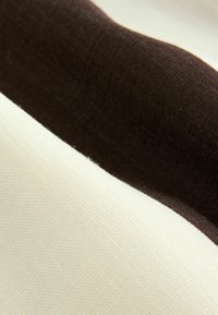 Tissu texturé avec des rayures crème et marron foncé, présentant une surface lisse avec des variations subtiles dans le tissage et le contraste des couleurs.