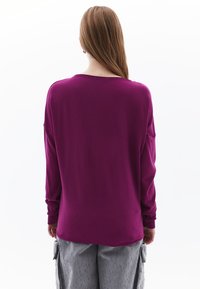 Pullover a maniche lunghe in tessuto viola scuro, caratterizzato da una vestibilità ampia, polsi a coste e un collo rotondo, con una texture liscia.
